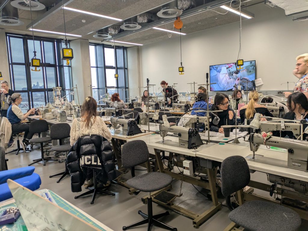 Photo of Jade's classroom with student's at sewing machines and the tutorial making task live on the screen